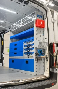 Close-up of the driver-side Syncro shelving, showing upper parts bins, open shelves at several heights, shallow and deep drawers, lower enclosed storage, a paper-roll holder, and rear-facing accessory mounting space.