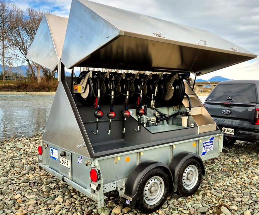 MecLube equipment in an Open mobile lube trailer with raised cover, multiple hose reels, fluid meters, storage compartments, and pickup truck beside a river.